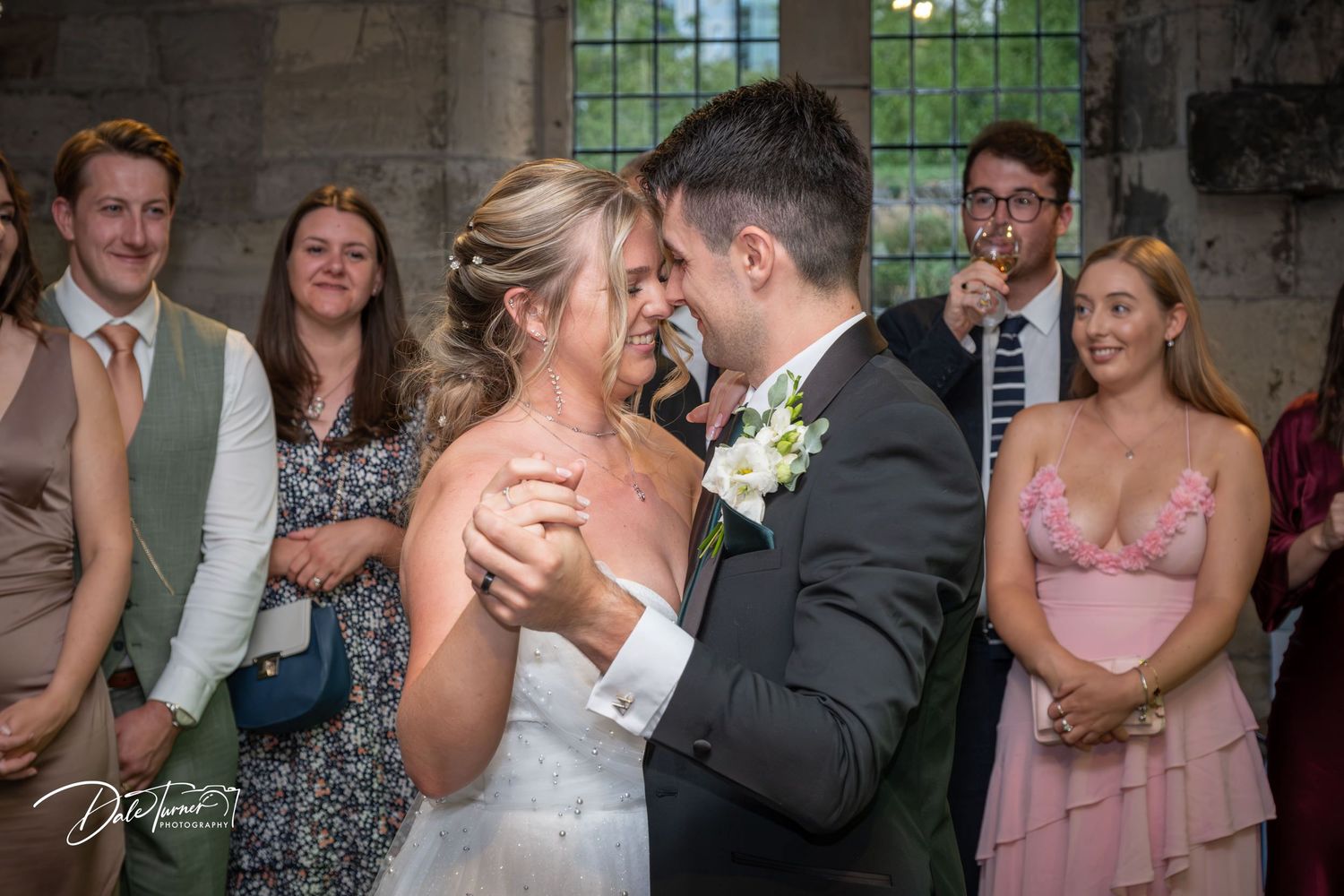 Newlyweds share an intimate moment during their first dance surrounded by wedding guests.