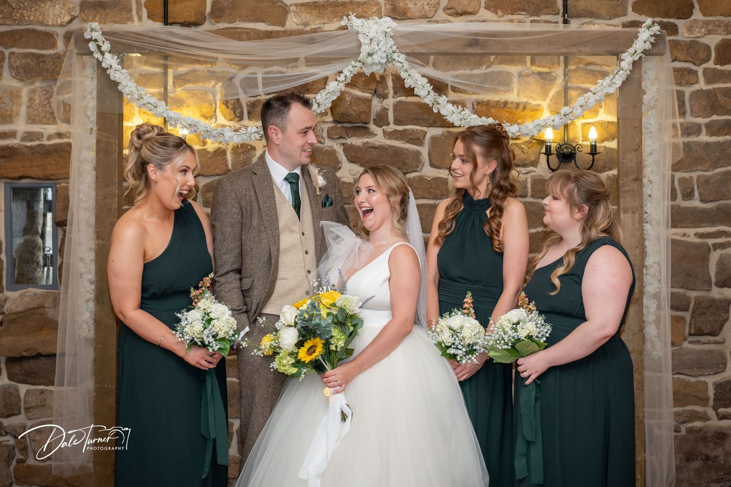 Wedding party celebrates in rustic stone venue with elegant decor and yellow floral bouquets.