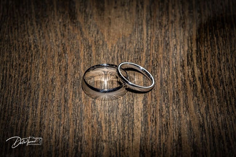 Wedding rings photographed on dark wooden surface with dramatic lighting.