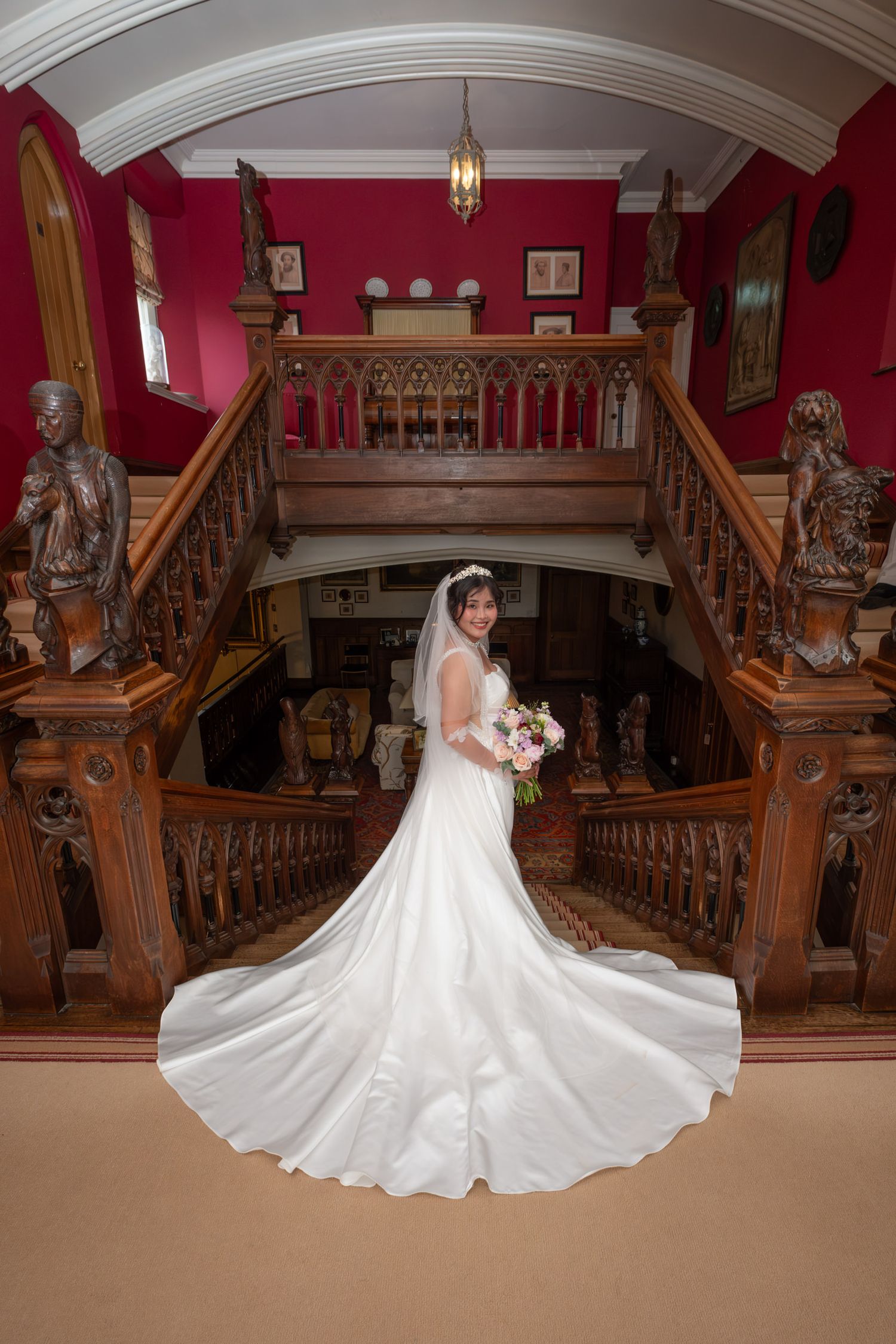 A stunning bridal portrait on a grand wooden staircase with red walls and ornate architectural details.