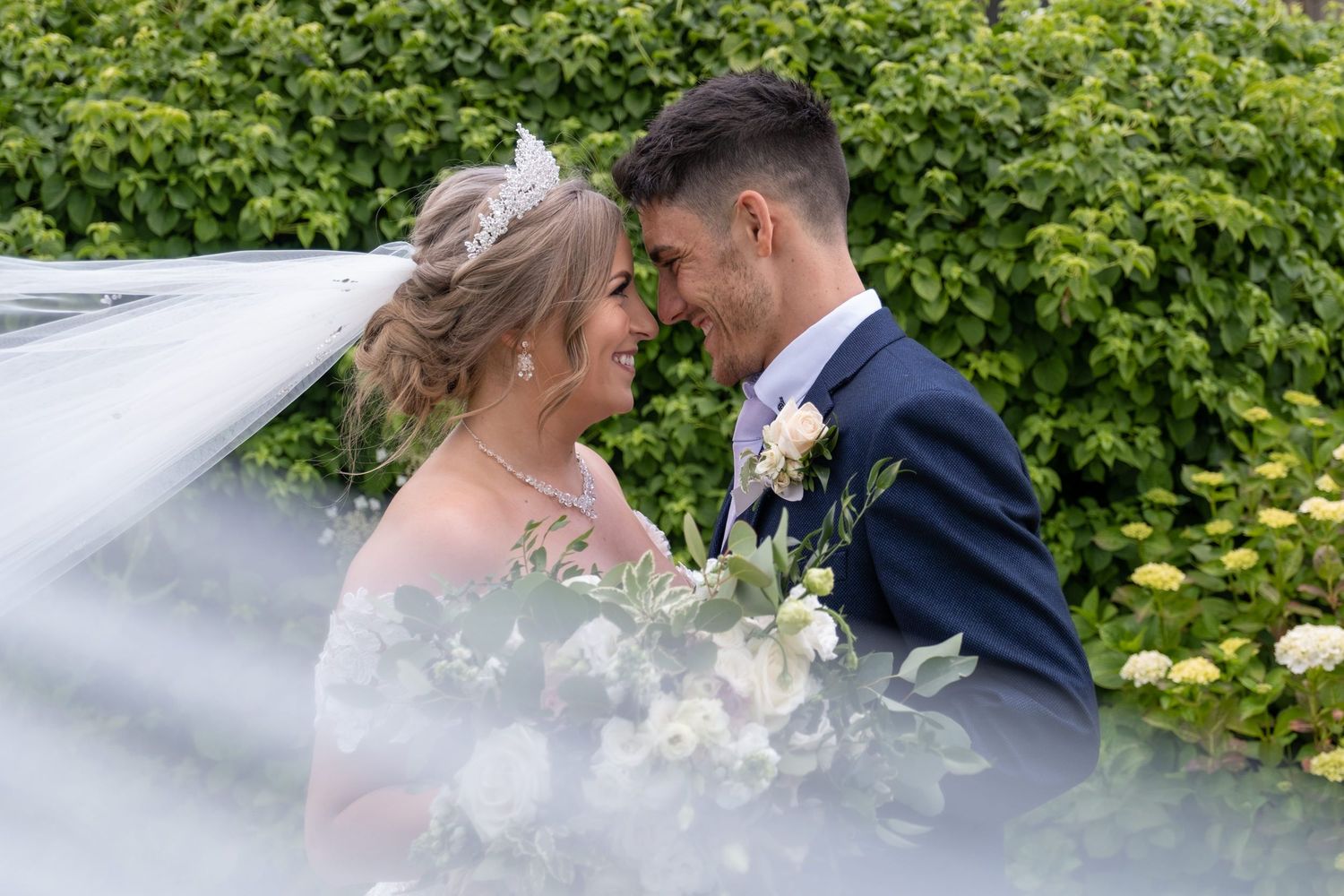 Intimate wedding portraits captured in a lush garden setting with white flowers.