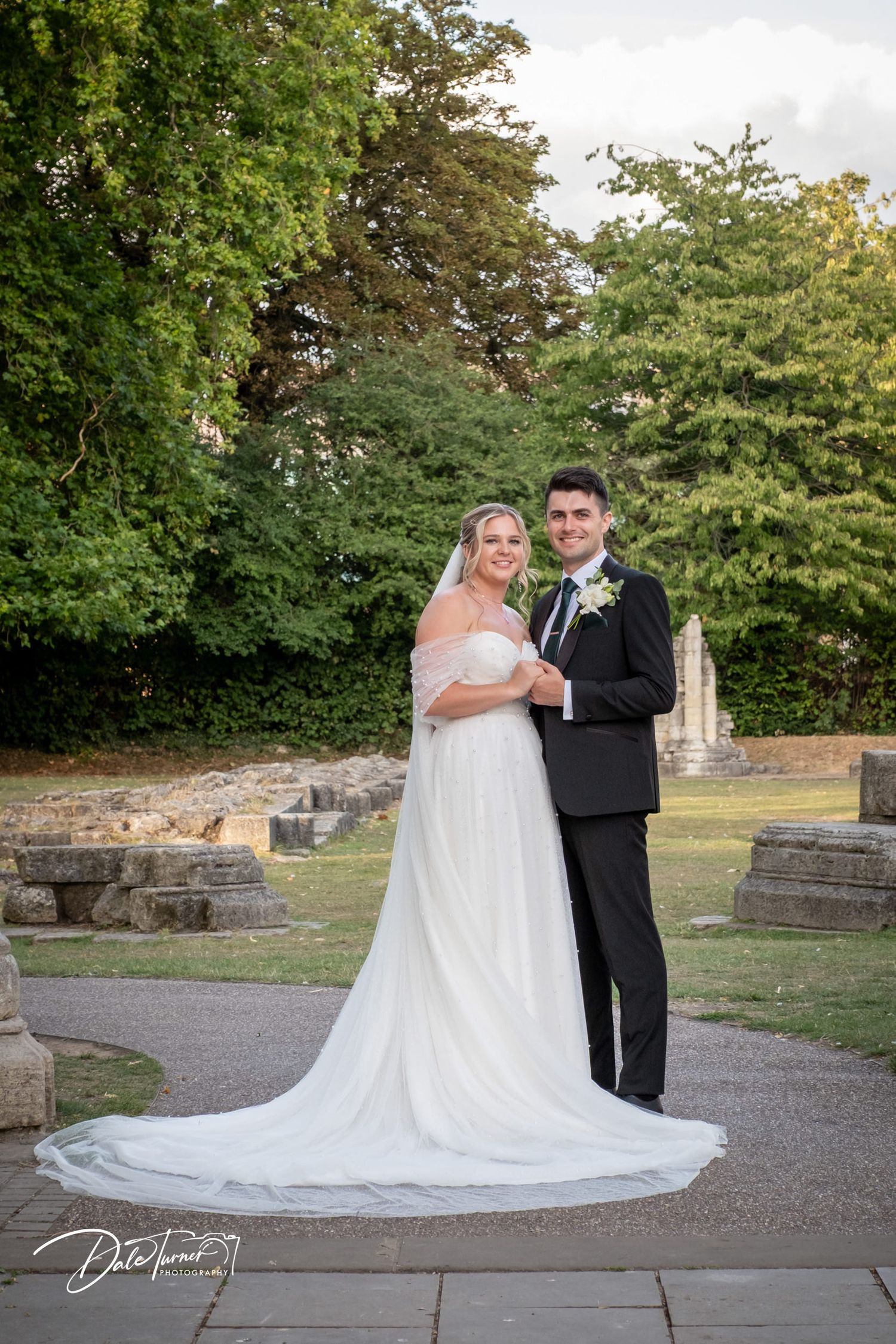 Elegant wedding portraits on stone pathway with cathedral train dress against garden backdrop.