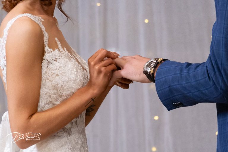 Wedding ceremony detail shots of hands exchanging rings against white backdrop.