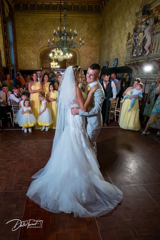 Wedding couple shares their first dance surrounded by guests in yellow dresses in an elegant ballroom.