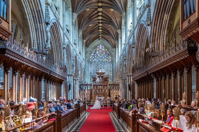Panoramic view of cathedral interior with gothic architecture and red carpeted center aisle.