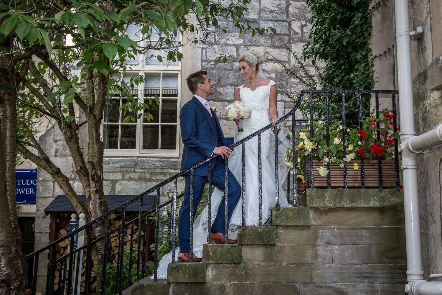 Wedding couple posing on stone steps with white railing and floral backdrop.
