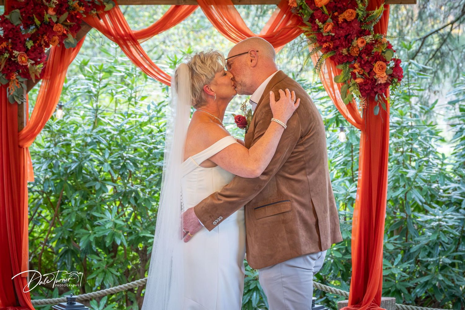 Wedding ceremony moment captured under an elegant red and floral decorated arch.