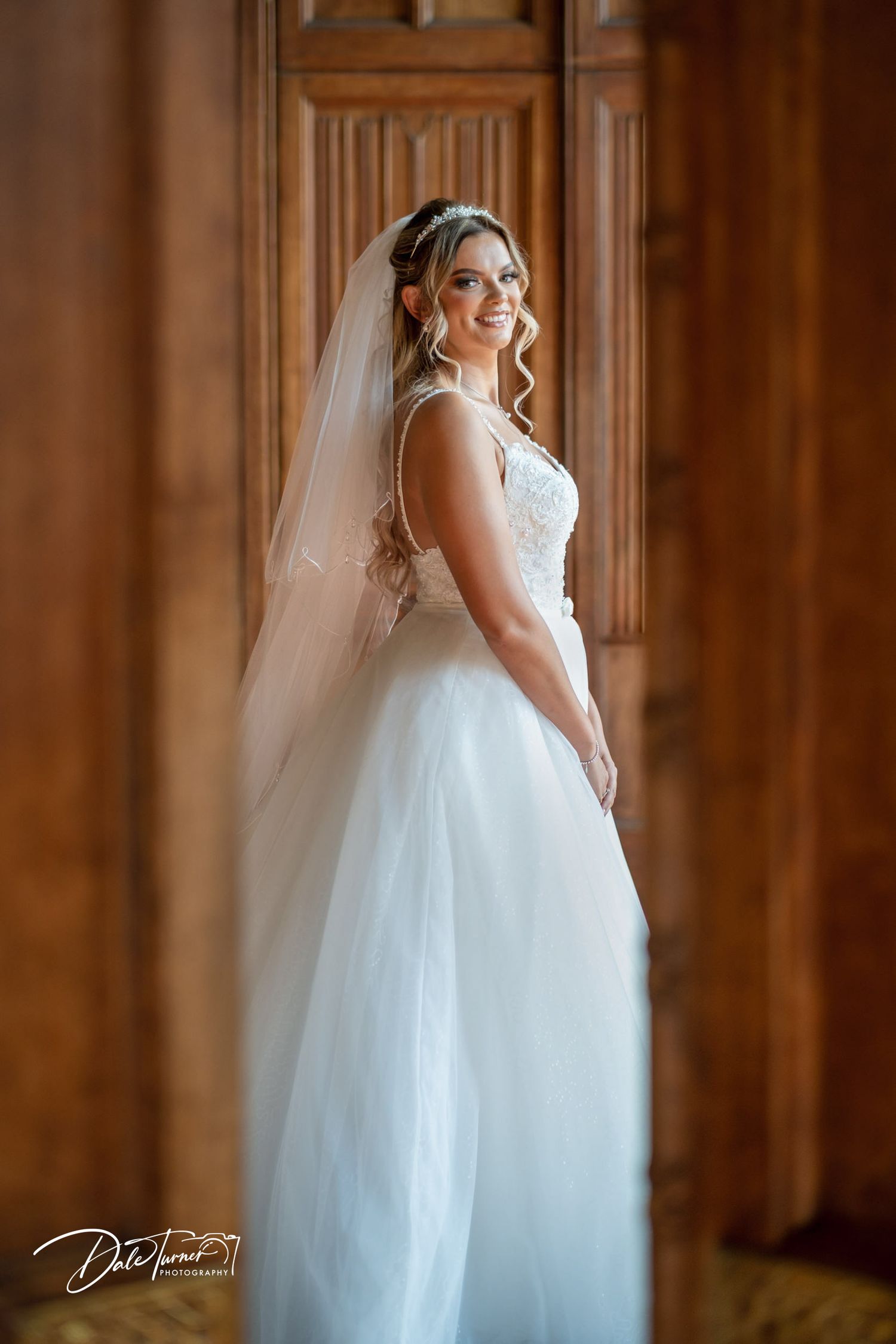 An elegant white wedding dress with tulle skirt displayed against rich wood paneled walls.