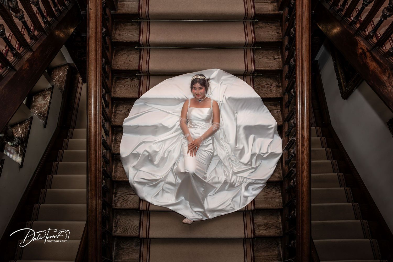 Wedding couple poses on elegant wooden staircase in romantic bridal photography session.