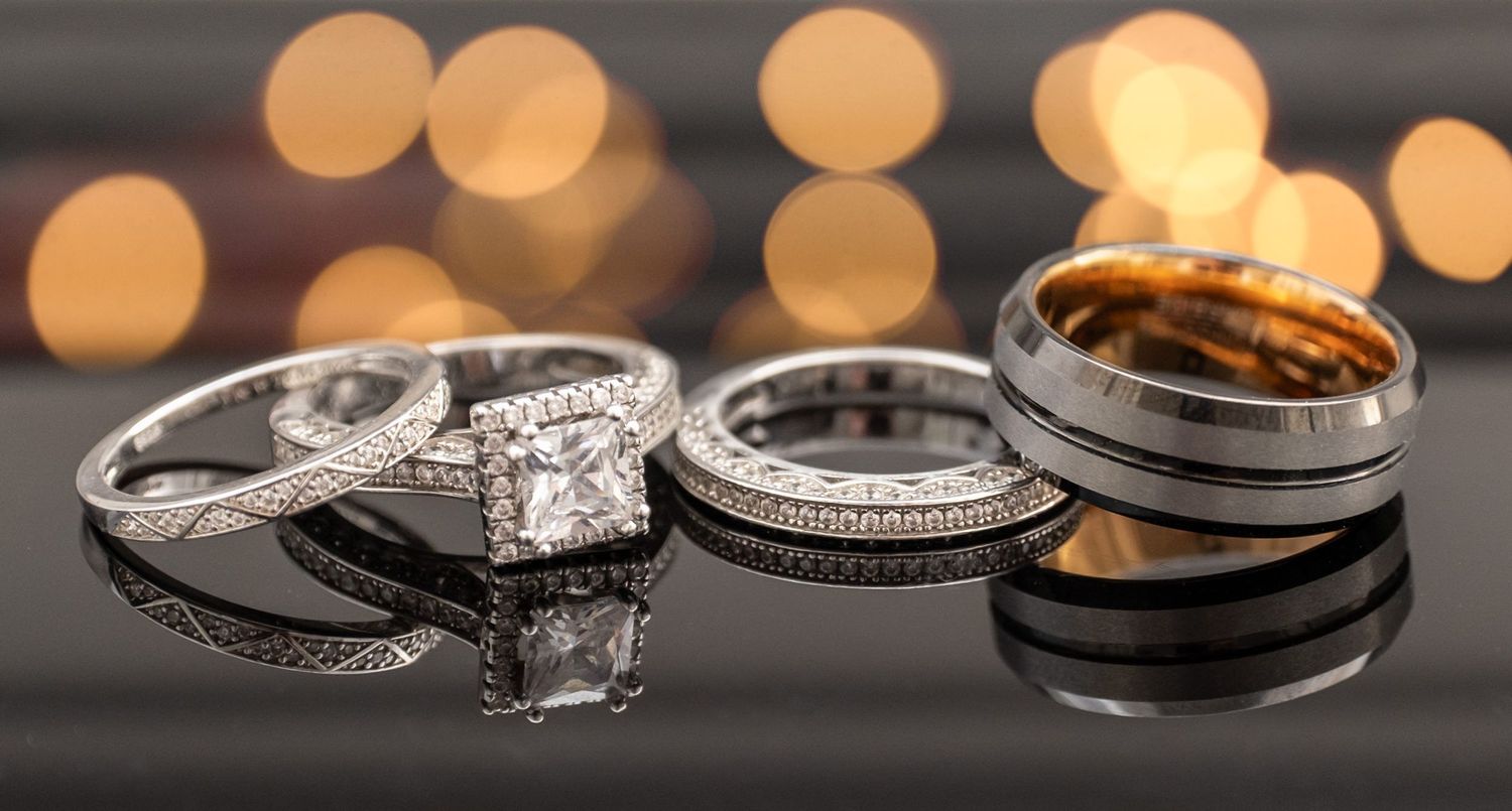 Close-up shots of elegant diamond wedding rings and bands arranged on a dark surface with soft bokeh lighting.
