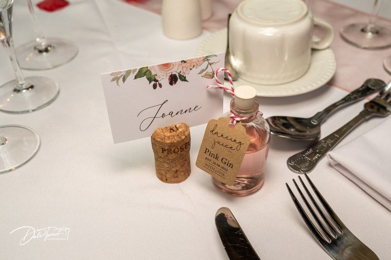 Close-up of formal place setting with wine glasses, silverware and rose petals on white tablecloth.