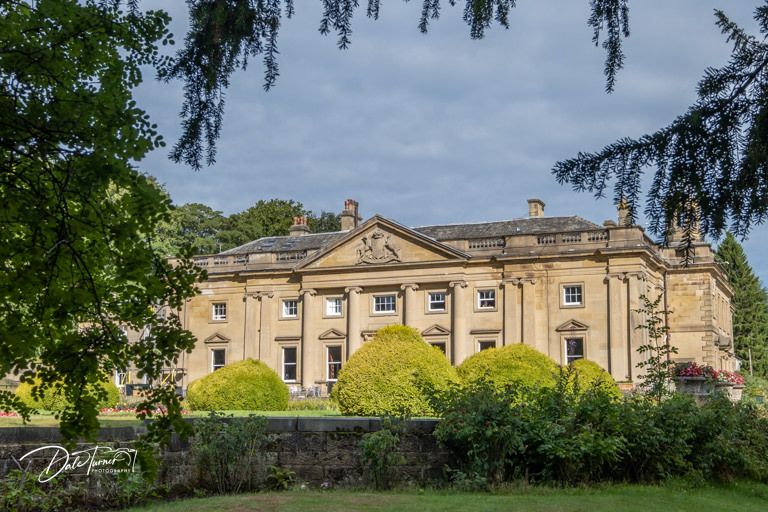 Elegant stone mansion with Georgian architecture and manicured gardens on a cloudy day.