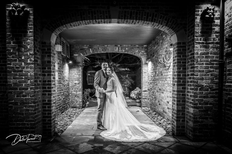 A wedding couple poses in a dramatic brick archway tunnel for a black and white portrait.