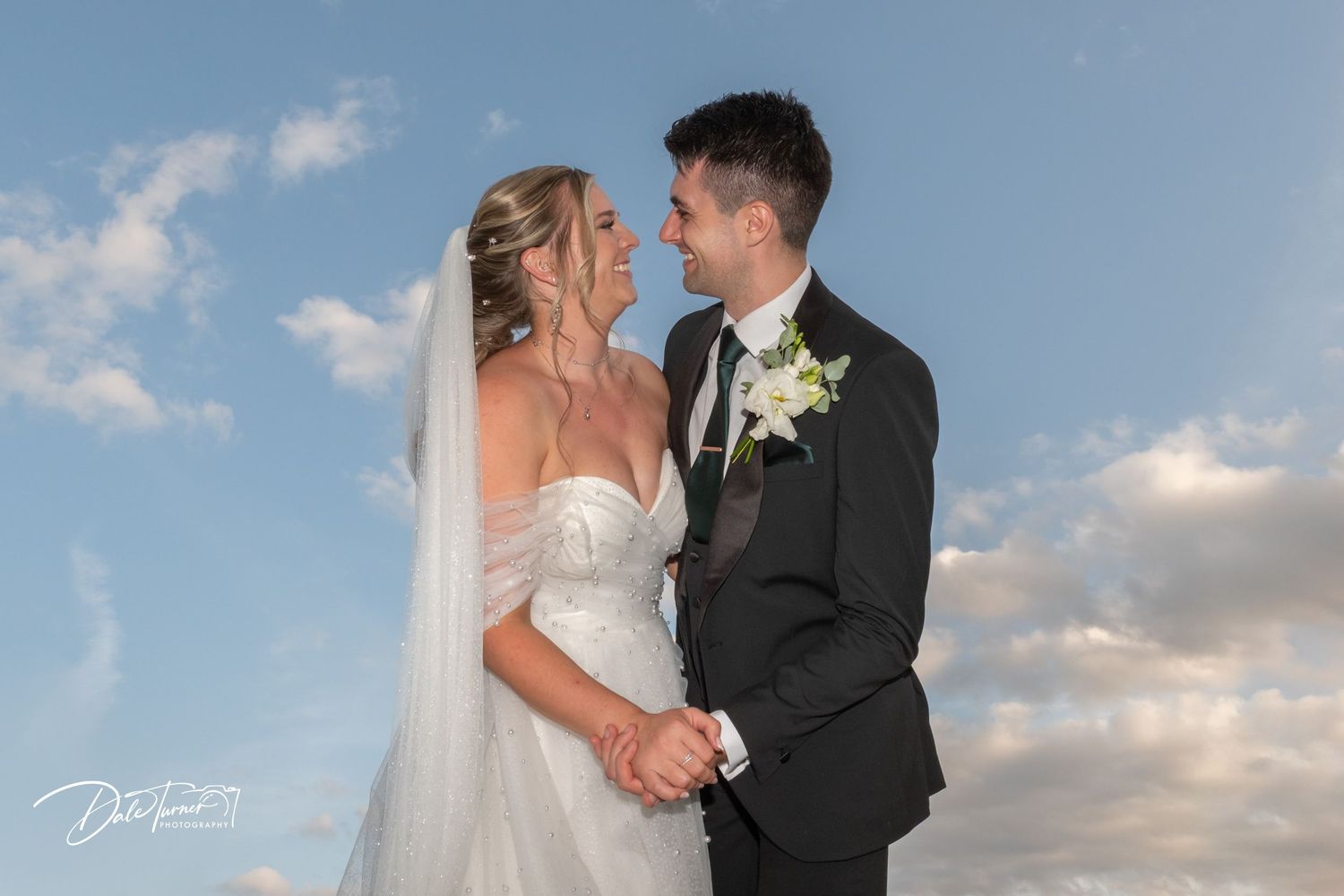 Wedding portrait against blue sky with soft clouds at golden hour.