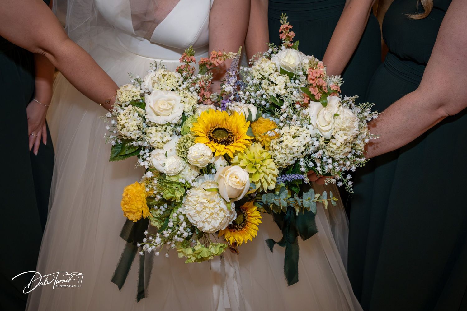 Wedding bouquets featuring sunflowers, white roses and wildflowers are displayed in a row against a dark background.