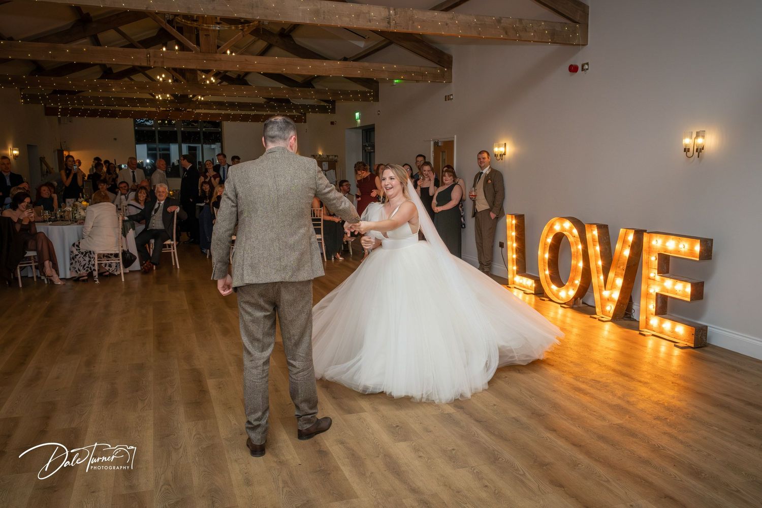 Wedding couple dances in front of illuminated LOVE sign during their first dance at an indoor reception venue.