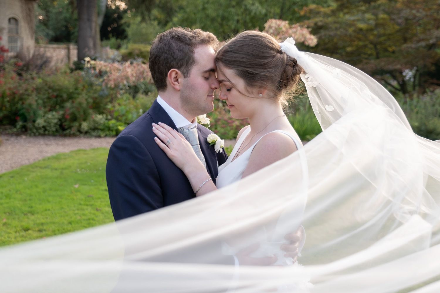 Flowing white wedding dress veil billowing dramatically in the breeze against a garden backdrop.