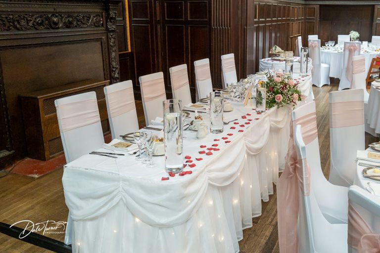 Wedding reception tables with white chair covers and elegant place settings in a grand ballroom.