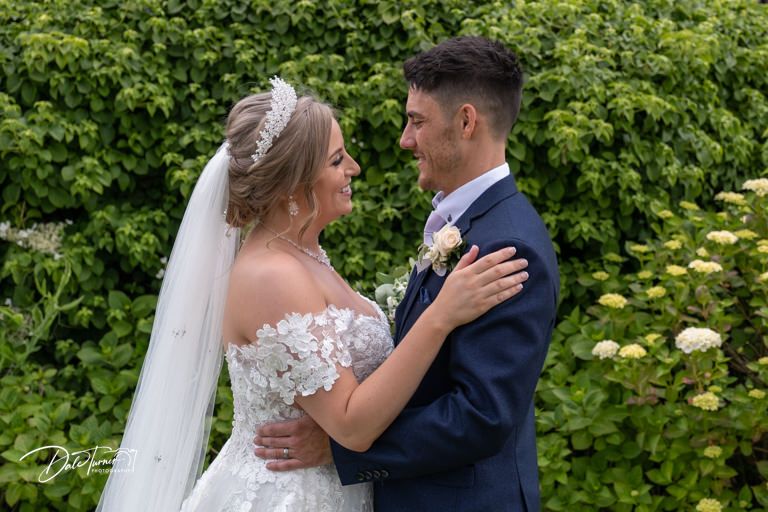 Wedding couple shares an intimate moment in a garden setting with lush greenery.