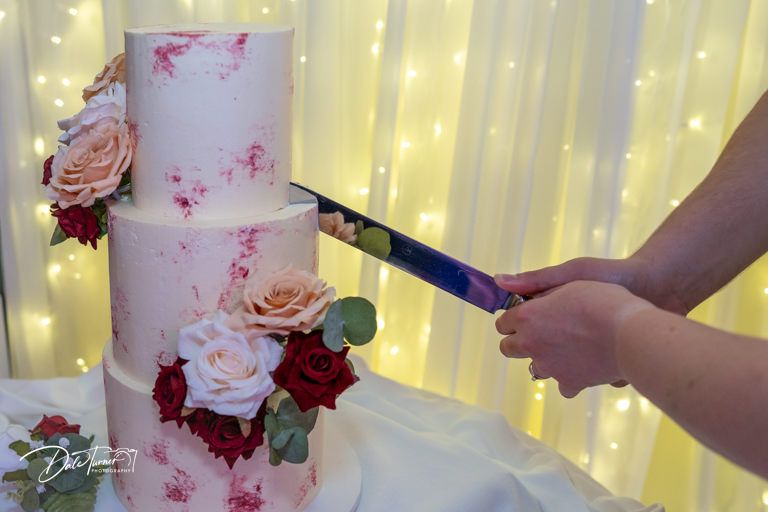 Wedding cake with delicate pink floral decorations against a backdrop of twinkling fairy lights.