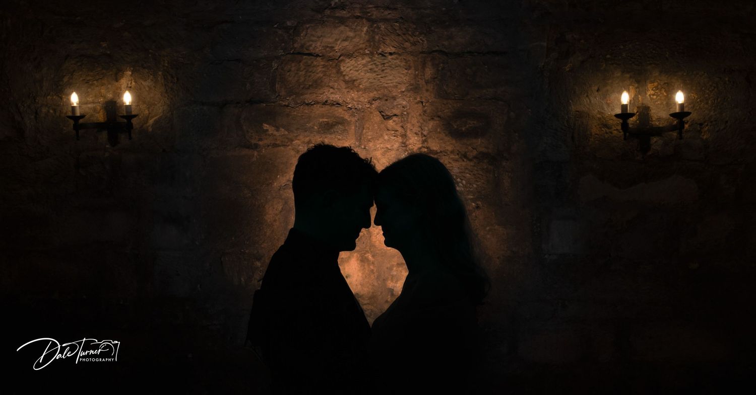Atmospheric wedding photos in a dimly lit stone corridor with wall sconces.