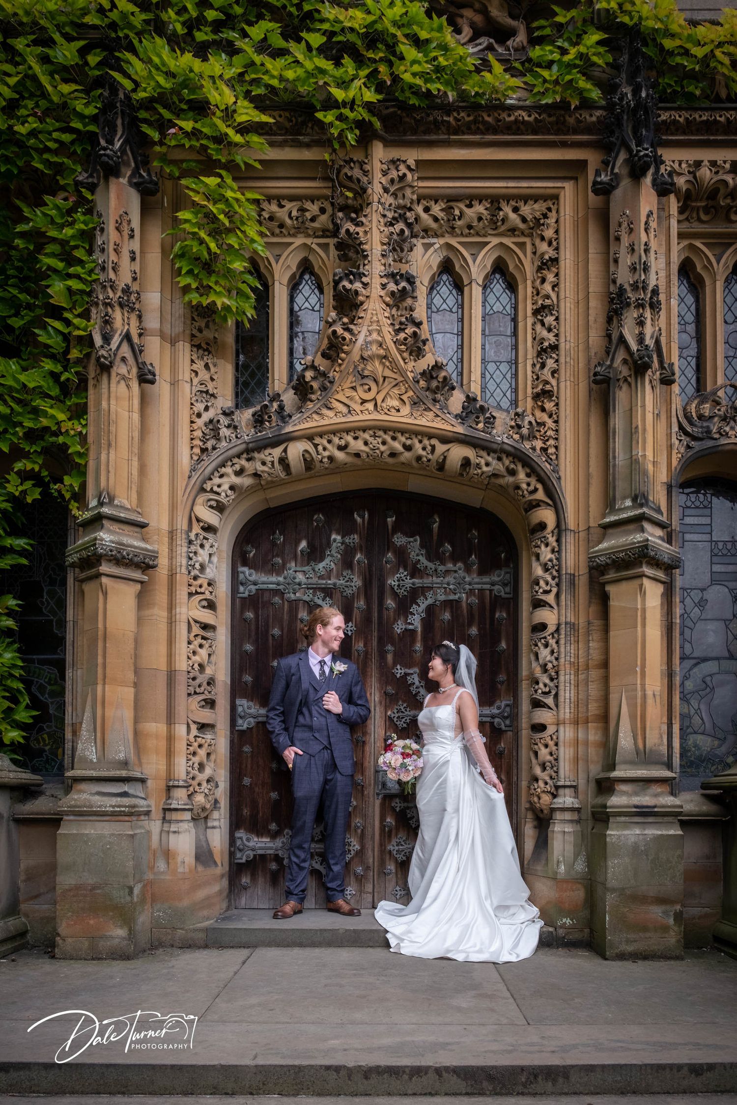 Wedding portraits captured under ornate Gothic archway with intricate stone carvings.