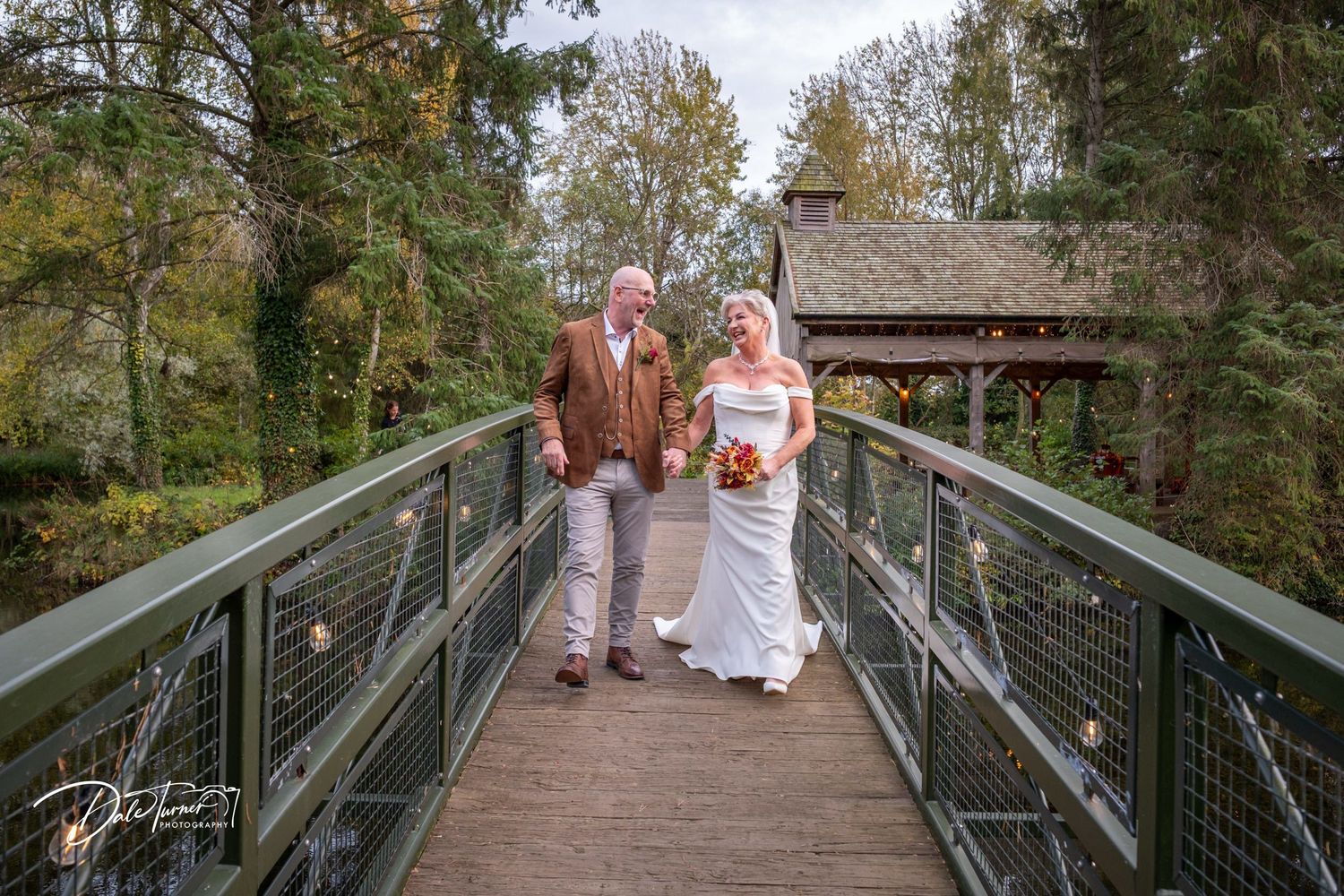 Elevated wooden walkway through autumn trees leading to wedding venue.