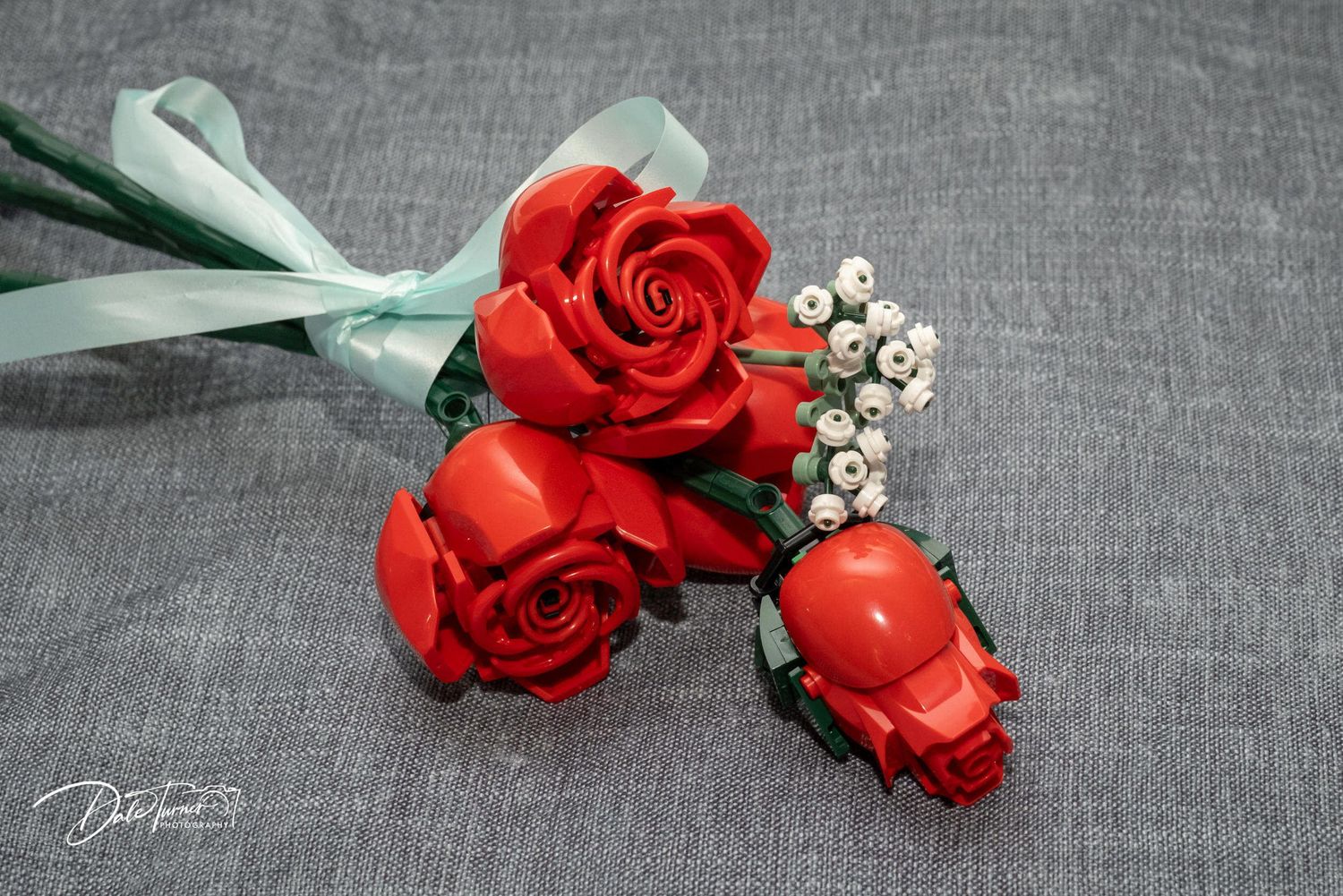 Red roses with baby's breath boutonnieres arranged on grey fabric background.