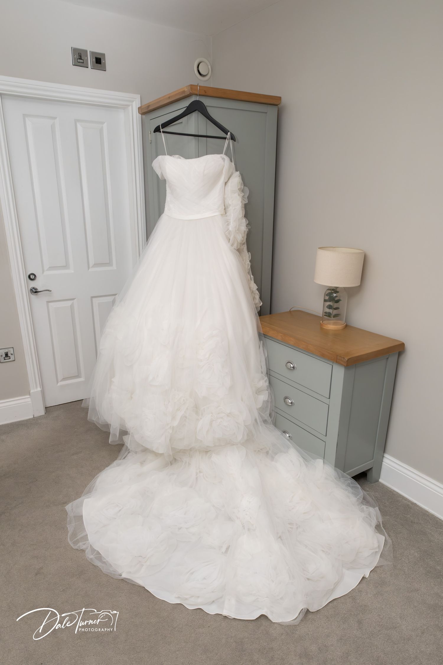 Elegant white ball gown wedding dress with ruffled train hanging on a wardrobe in a bridal suite.