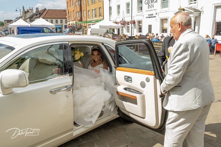 White vintage wedding car parked outside historic buildings.