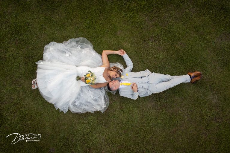Artistic overhead view of white wedding dress spread out on dark grass.
