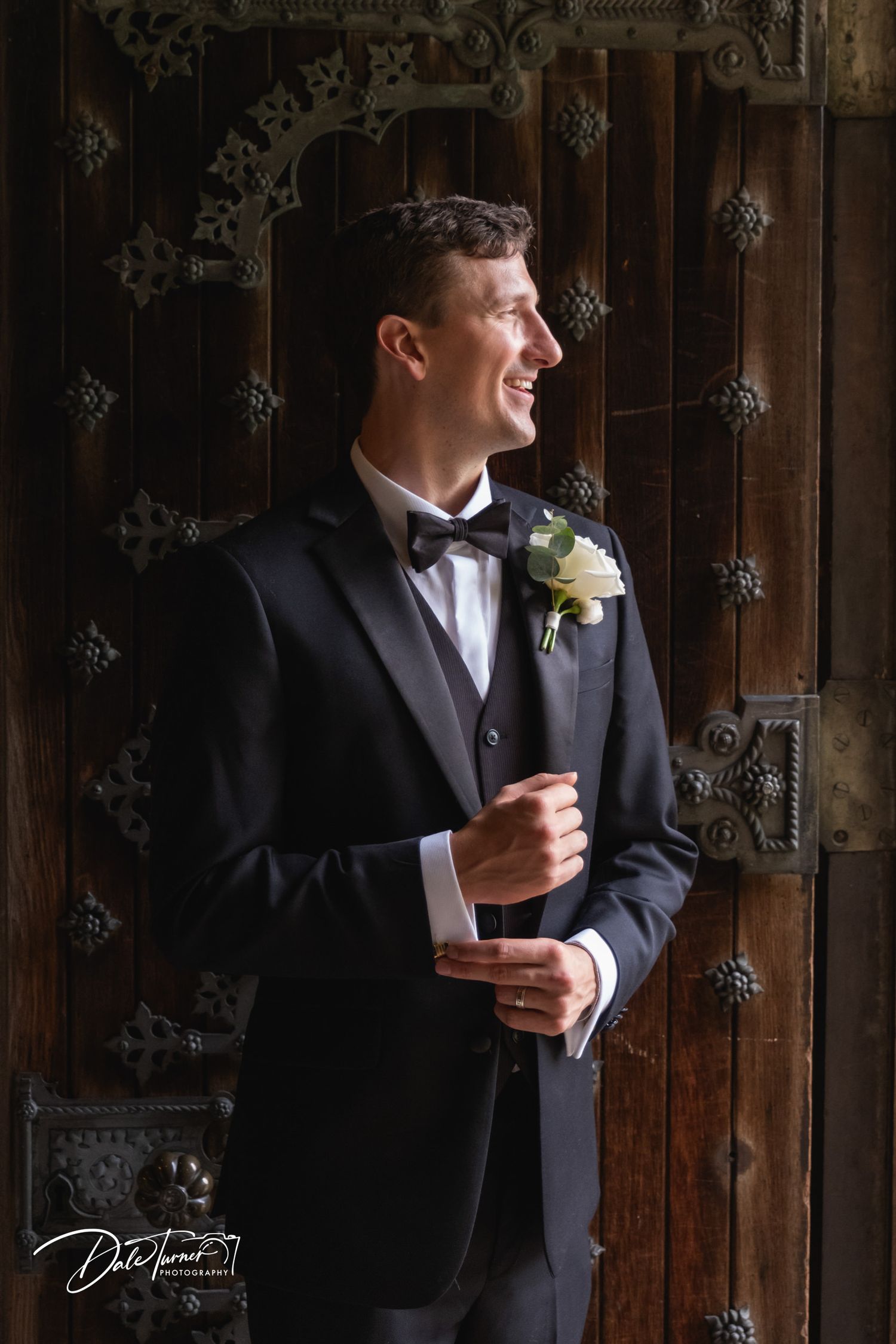 Moody portrait against dark wooden door with ornate metalwork details.