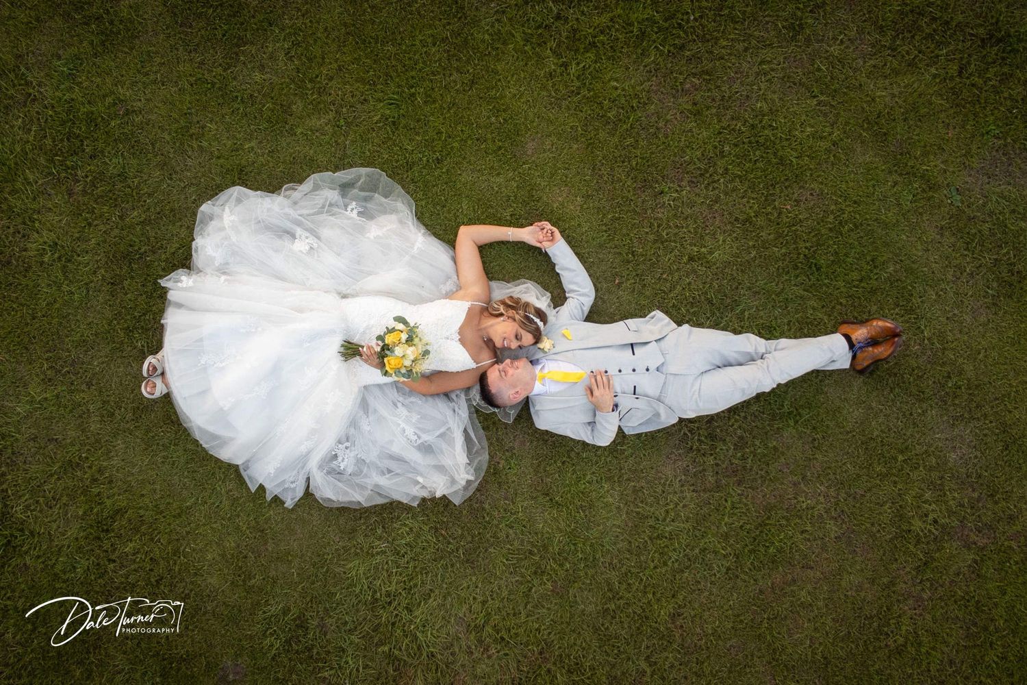 A bride in white dress lying on green grass creating artistic wedding photography.