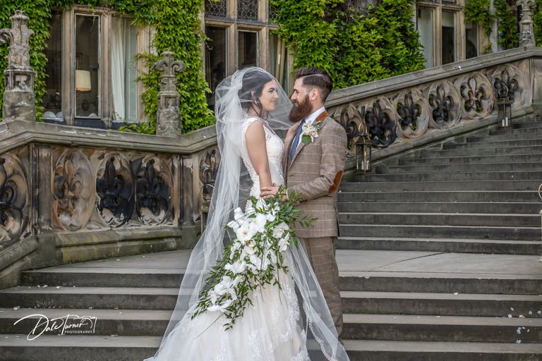 Romantic moment captured on decorative stone steps with ivy-covered walls.