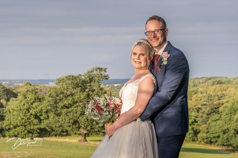Newlyweds pose together on hilltop with scenic countryside views.