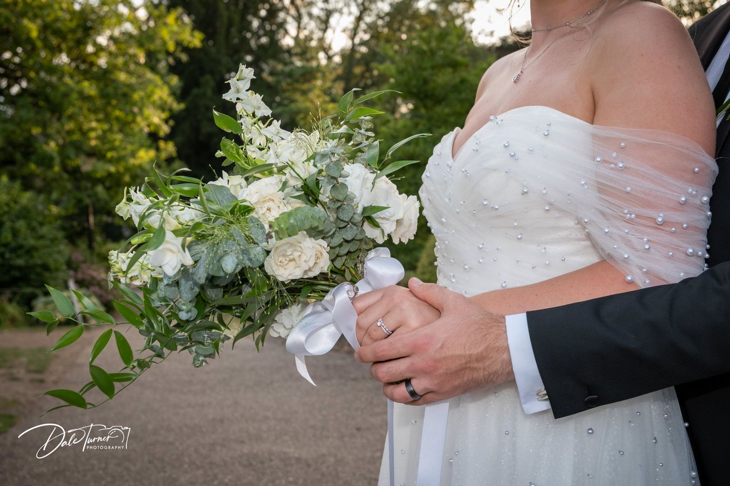 Close-up of an elegant white and green wedding bouquet being held against a white dress.