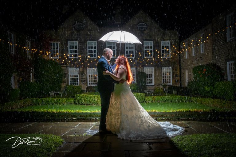 Elegant nighttime wedding photos taken under a white umbrella against a historic building backdrop.