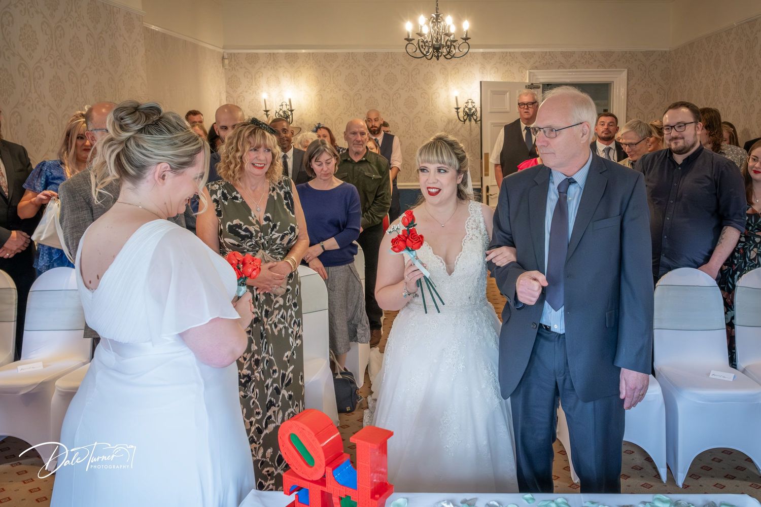 Wedding ceremony in progress inside an elegant room with white chair covers.
