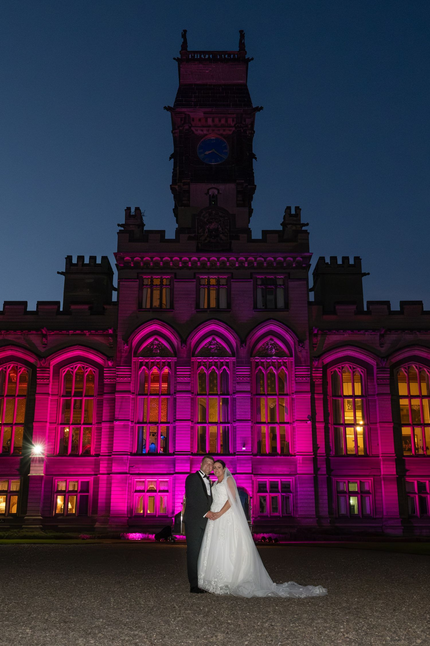 A historic building illuminated in vibrant pink lighting creates a dramatic nighttime wedding backdrop.