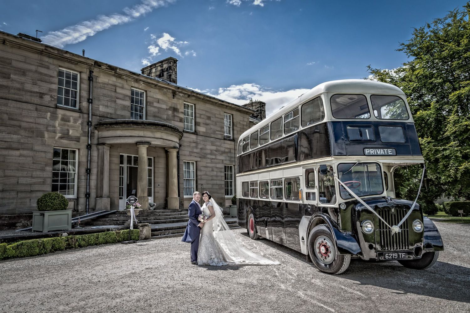 Vintage buses parked outside a historic stone building on a sunny wedding day.