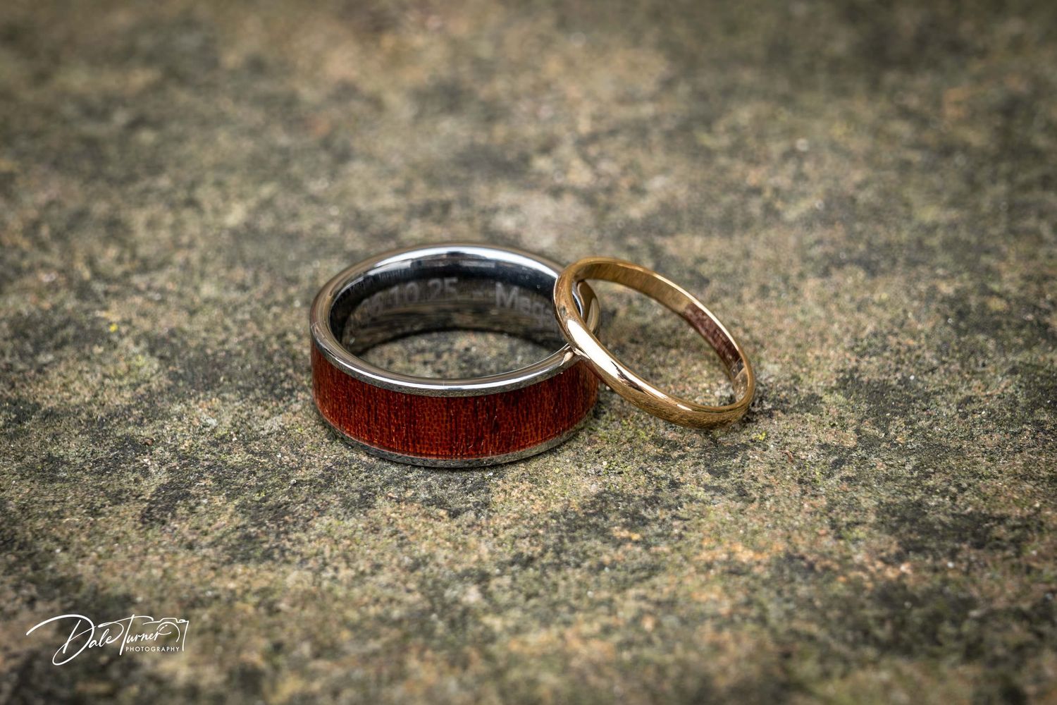 Close-up view of wedding rings on a textured stone surface in natural lighting.