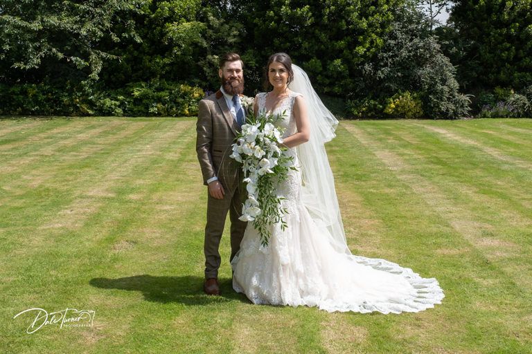 Newlyweds pose for portraits on manicured lawn of historic venue.