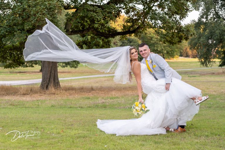 Wedding couple posing in a scenic field with flowing white dress and natural backdrop.