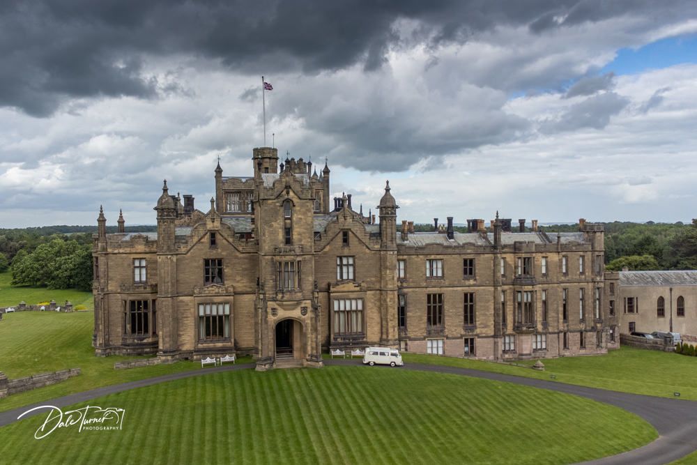 Dramatic panoramic view of a grand historic castle estate under moody storm clouds.