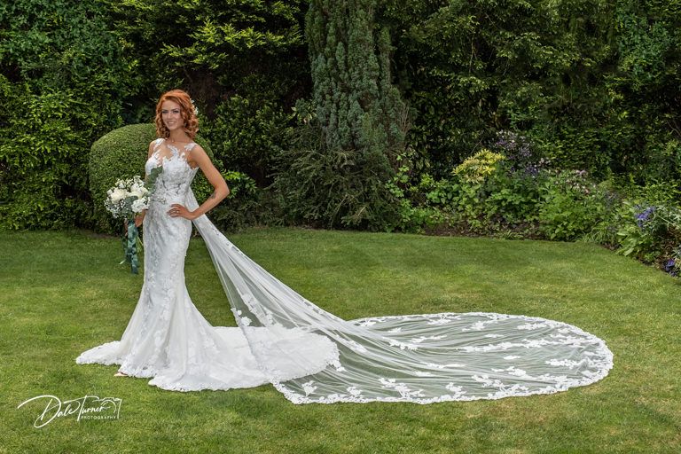 Bride with flowing cathedral veil poses gracefully in garden setting.