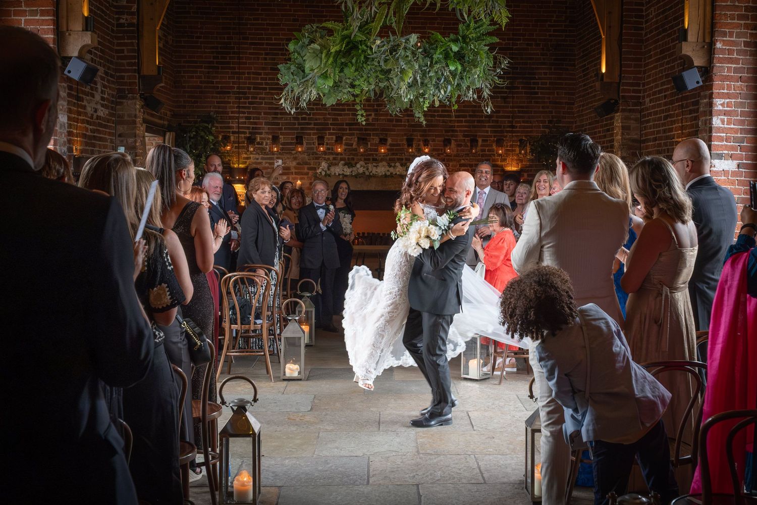 Wedding reception guests dancing and mingling in a rustic brick venue with warm lighting.