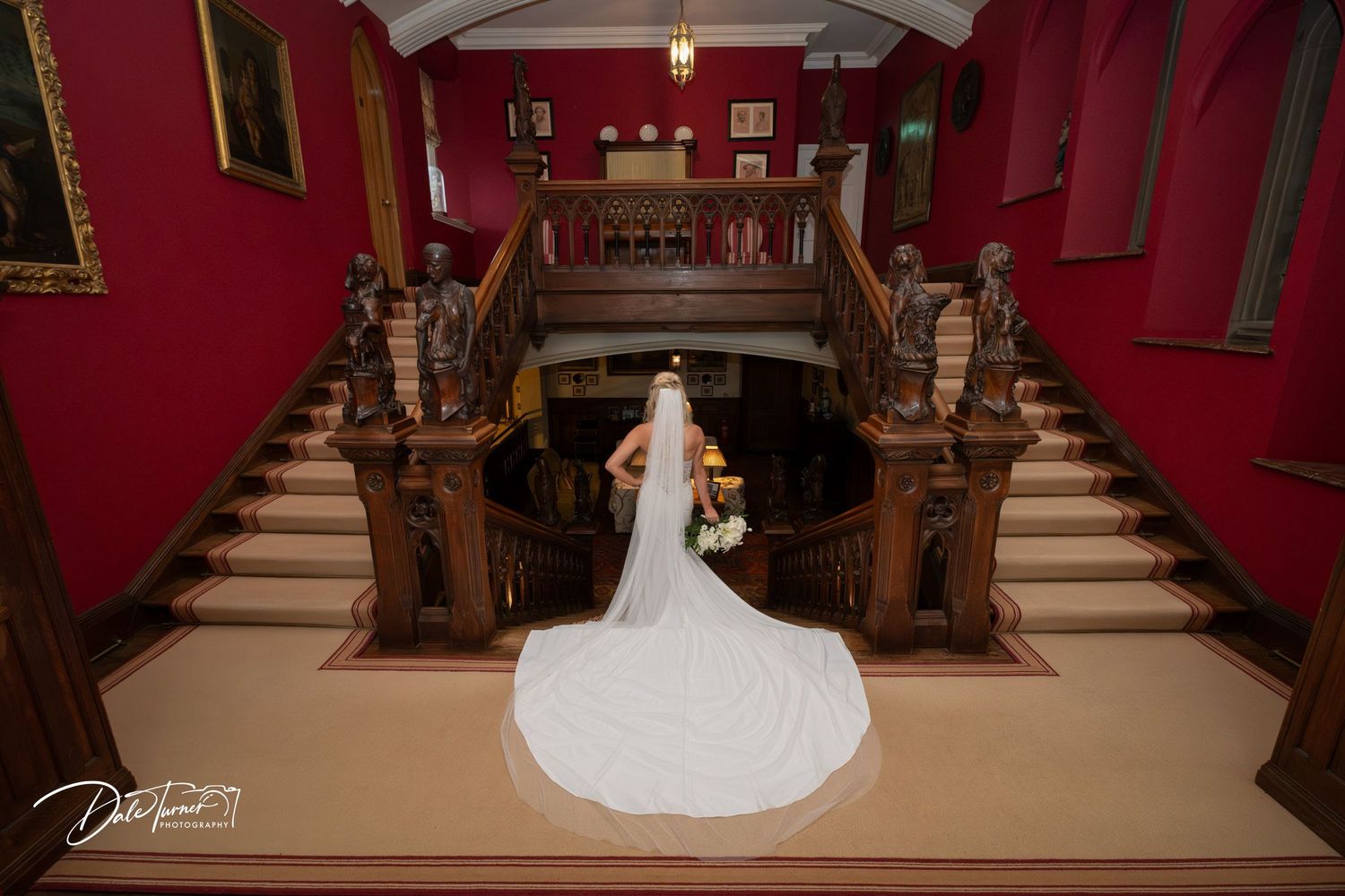 Grand staircase with red walls and wooden banisters in an elegant historic building interior.