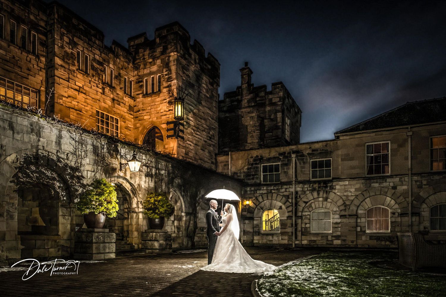 Dramatic nighttime wedding photos captured at an illuminated stone castle with moody sky.