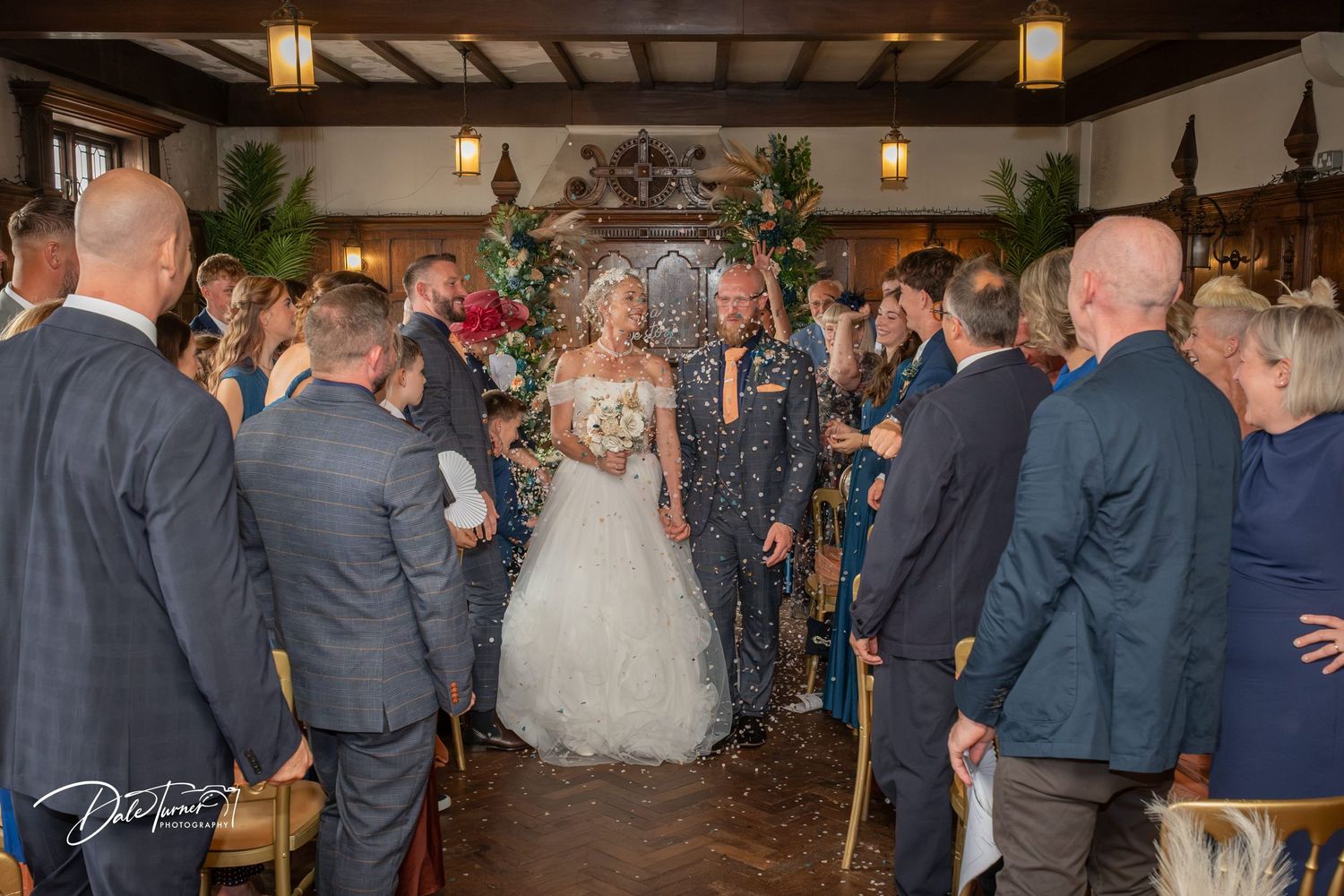 Bride and groom walk down the aisle together at an elegant indoor wedding ceremony with guests watching.