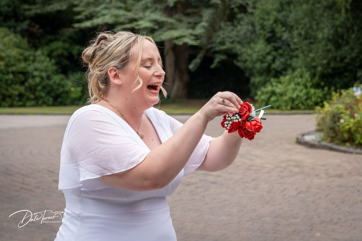 Person in white dress holding red flowers against outdoor backdrop.